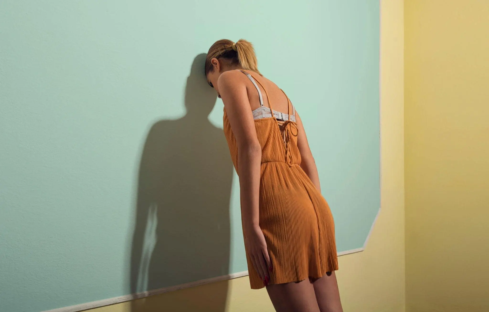 A poignant image of a woman leaning her head against a pastel-colored wall, capturing the emotional weight and frustration that often comes before the moment of release. Letting go isn't about avoiding feelings; it's about confronting them and choosing to move forward.